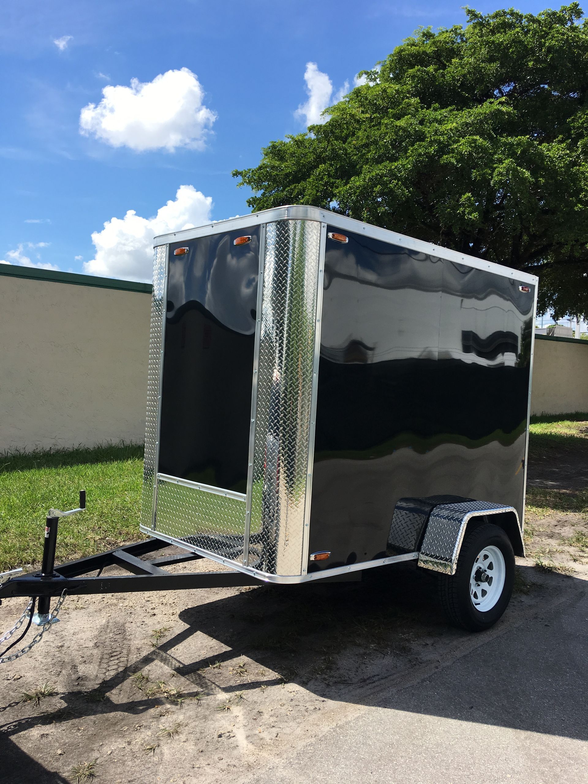 Black enclosed cargo trailer parked outdoors on a sunny day, with silver trim and a white wheel.