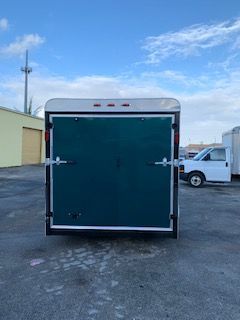 White enclosed cargo trailer with rear double doors parked in a lot under a blue sky