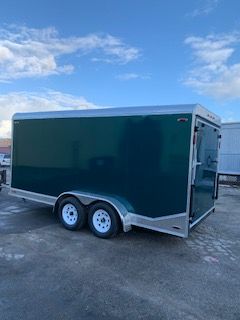 Green enclosed dual-axle cargo trailer on a paved lot under a partly cloudy sky