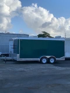 Green enclosed trailer parked on a paved lot under a cloudy sky