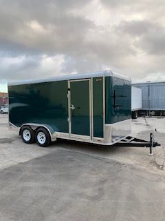 Green enclosed dual-axle cargo trailer parked on a concrete lot under cloudy sky