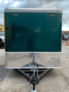 Green enclosed utility trailer with silver trim and a hitch, parked on pavement.