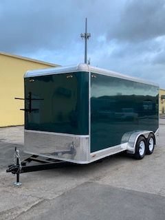 Dark green enclosed dual-axle cargo trailer parked beside a yellow building.