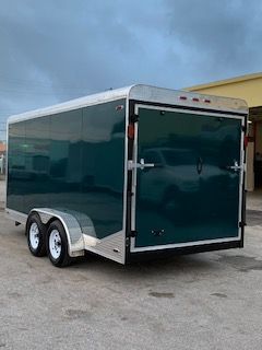 Green dual-axle enclosed cargo trailer parked on pavement under a cloudy sky