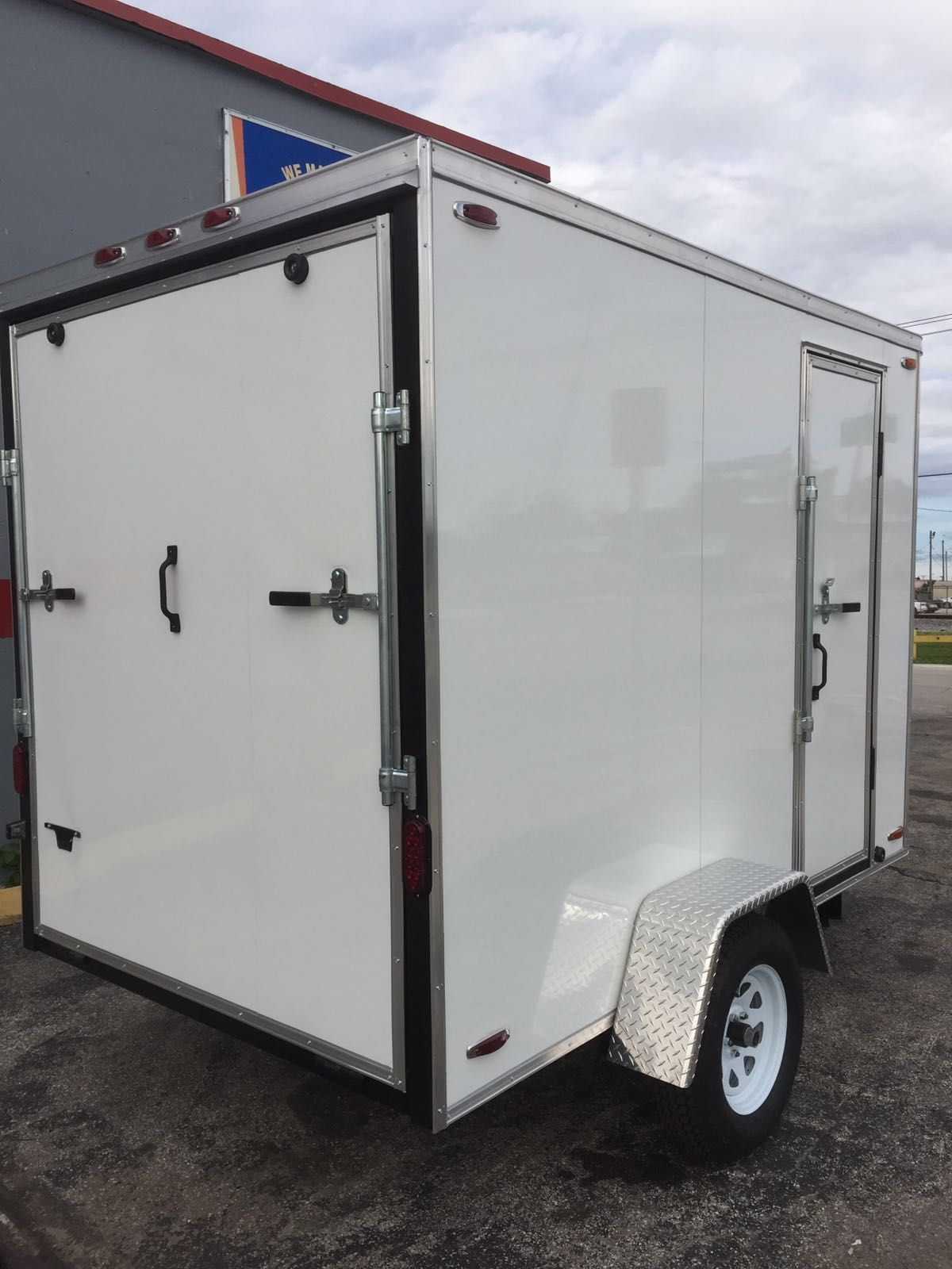 White enclosed cargo trailer with side door and wheel fender, parked outdoors on pavement