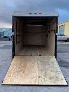Open cargo trailer with ramp lowered, viewed from the rear in a parking lot.