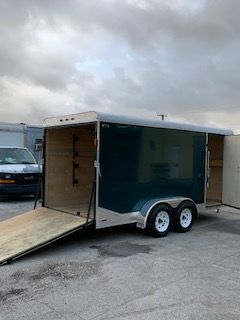 Dark green enclosed cargo trailer with open ramp door in a parking lot under cloudy skies