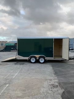 Green enclosed cargo trailer with open rear ramp, parked on a lot under cloudy skies