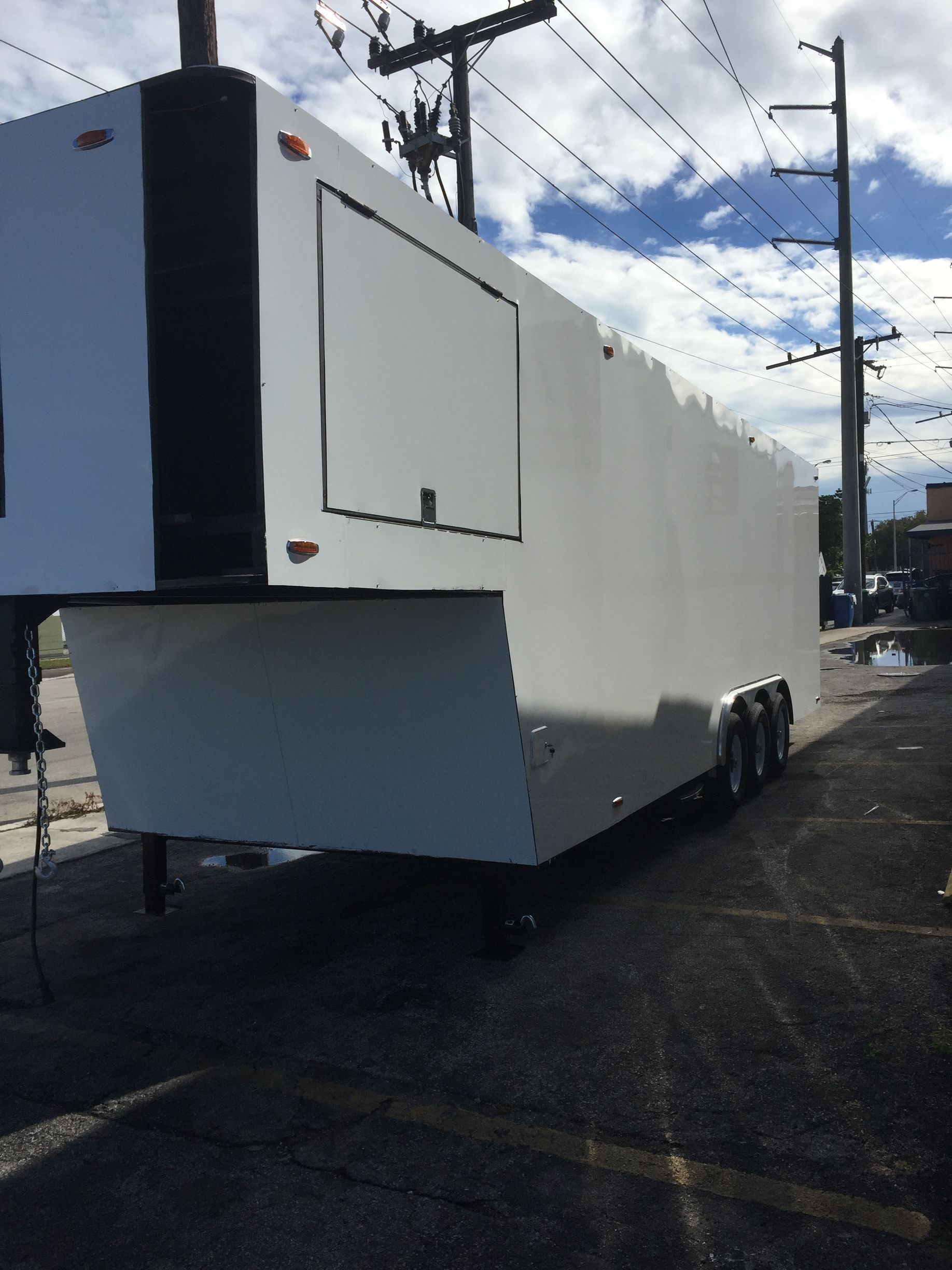 White utility trailer parked on a lot under a cloudy sky, viewed from the rear corner.