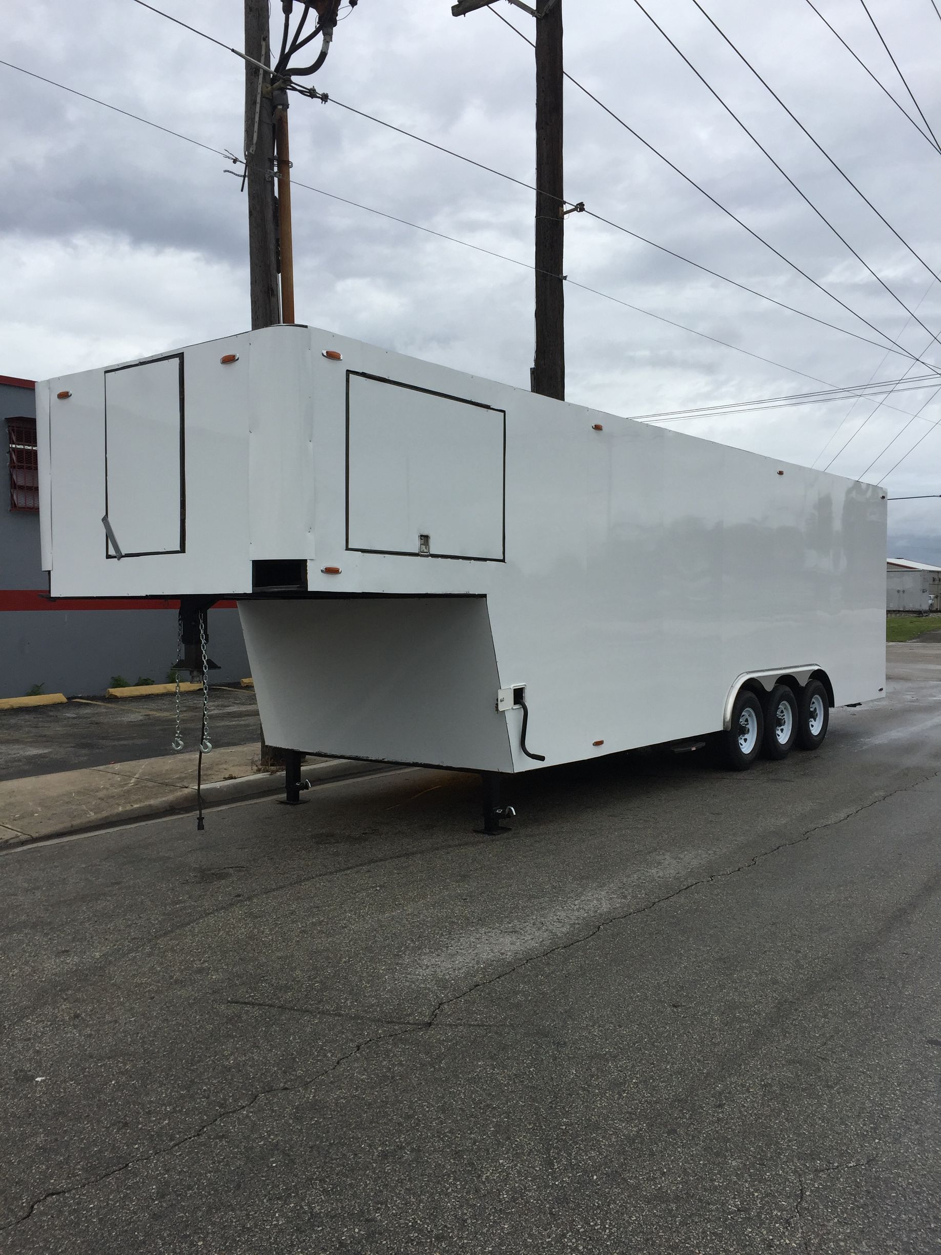 White two-axle semi trailer with open front compartments parked on a wet roadside under power lines