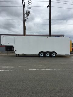 White enclosed trailer with three axles parked on a road under a cloudy sky.