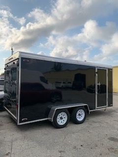 Black enclosed cargo trailer with tandem axles parked on a concrete lot under a cloudy sky
