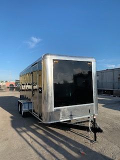Silver enclosed trailer parked on gravel lot under a clear blue sky