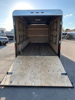 Open cargo trailer with lowered ramp and plywood floor, parked in a lot