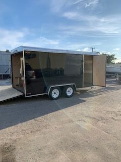Black enclosed cargo trailer with open rear doors parked on a paved lot under a blue sky