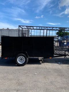 Black enclosed utility trailer parked on pavement in an industrial lot with metal framework in the background