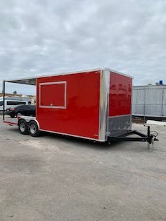 Red enclosed cargo trailer with a side door parked on a lot under cloudy skies.