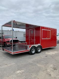 Red enclosed utility trailer with open front deck, parked on pavement near a truck under cloudy sky