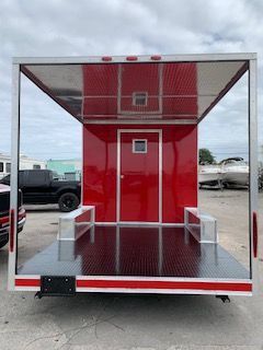 Red enclosed cargo trailer with open rear ramp and diamond-plate floor in a parking lot.
