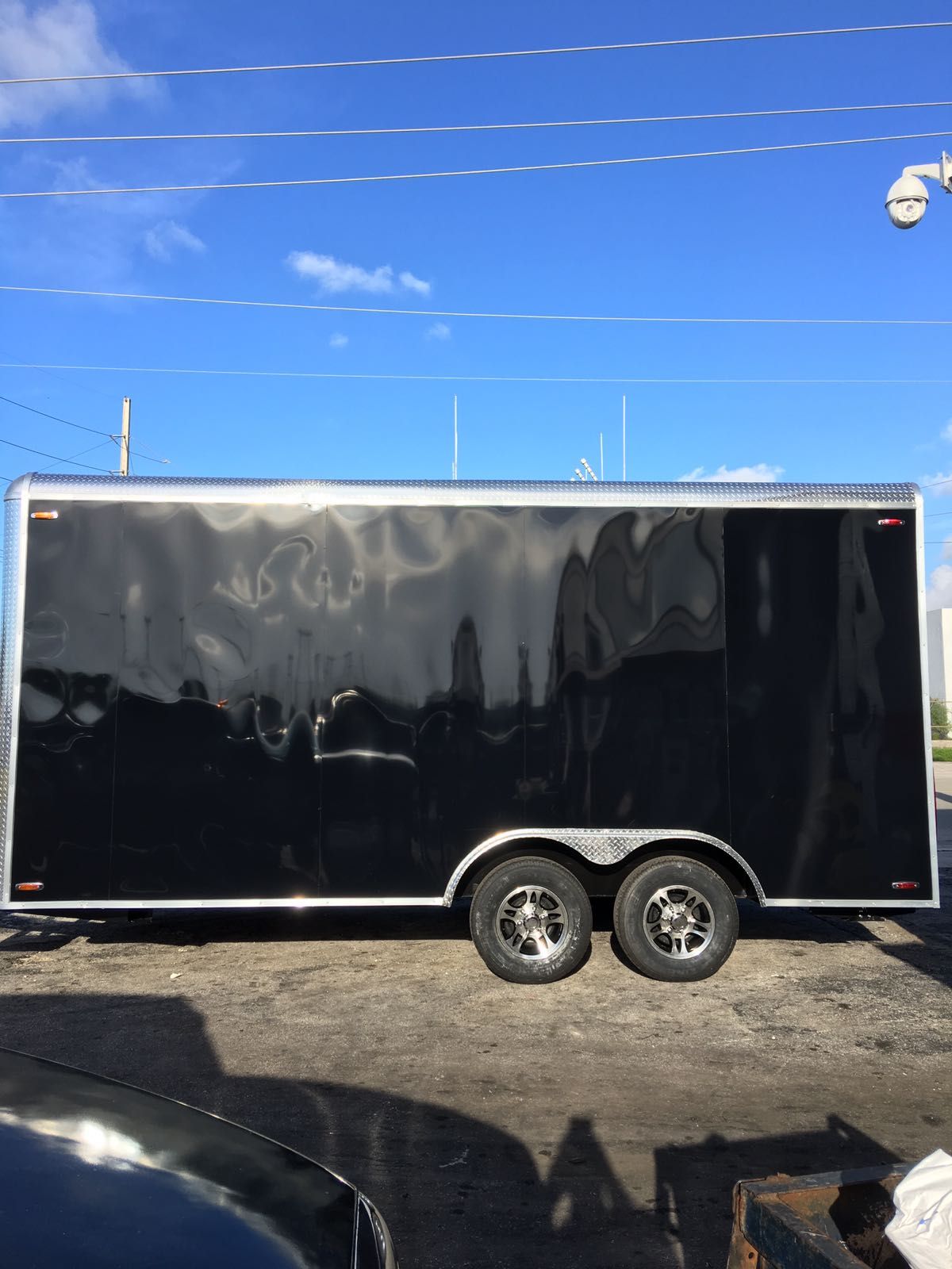 Black dual-axle cargo trailer parked in a lot under a clear blue sky.
