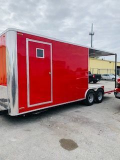 Red enclosed cargo trailer parked outdoors on asphalt, with a side door and tandem axles.