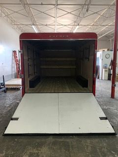 Open truck trailer with lowered white ramp inside an industrial warehouse