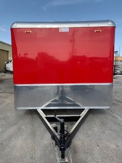 Red and silver enclosed trailer front view with hitch, parked on pavement outdoors
