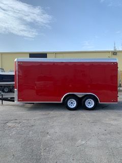 Red enclosed trailer with dual axles parked outside a building under a blue sky