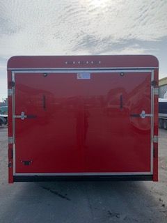 Red enclosed trailer with rear double doors, parked on pavement under a cloudy sky.