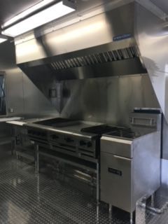 Stainless steel commercial kitchen range and ventilation hood in a restaurant prep area