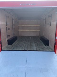 Empty red delivery truck cargo area with wooden floor and shelves, viewed from the open rear.
