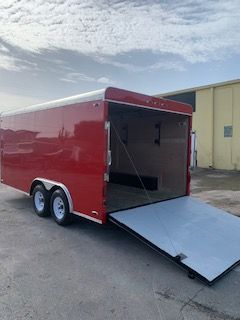 Red enclosed cargo trailer with rear ramp door open on a paved lot