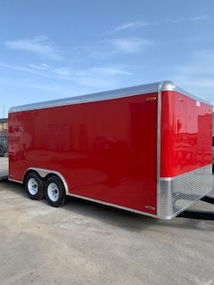 Red enclosed cargo trailer with silver trim and twin axles parked outdoors under a blue sky