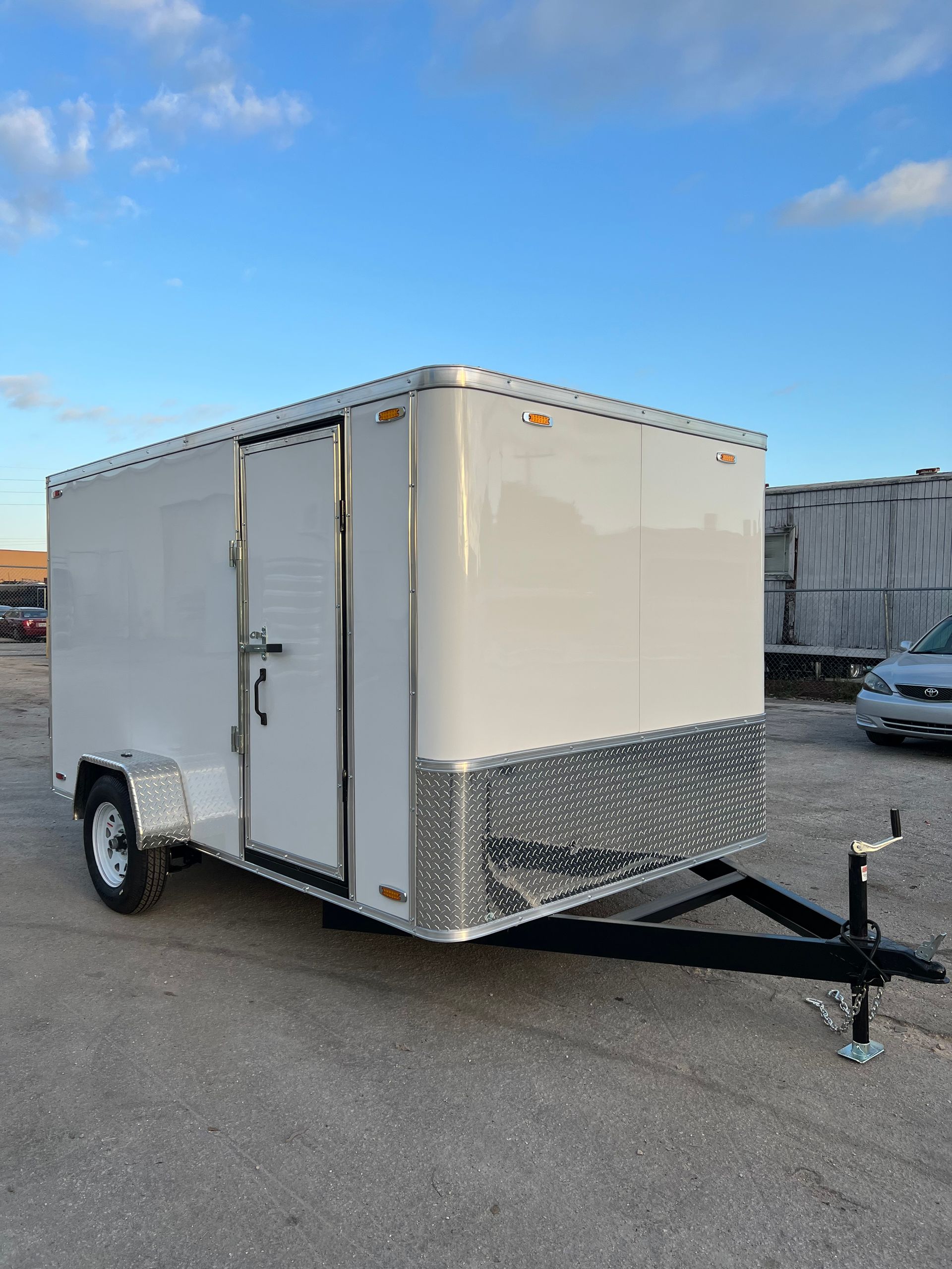 White enclosed cargo trailer with a side door and front hitch parked in a lot.