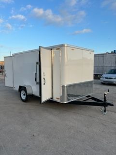 White enclosed cargo trailer with open side door and ramp parked on pavement under a blue sky