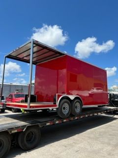Red enclosed trailer with open side frame on a flatbed truck under a blue sky