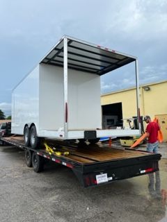 White box trailer on a flatbed trailer outside a warehouse, with a man loading it.