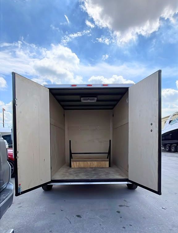Open truck trailer with rear doors wide open, showing an empty beige interior and bench seat under a cloudy sky