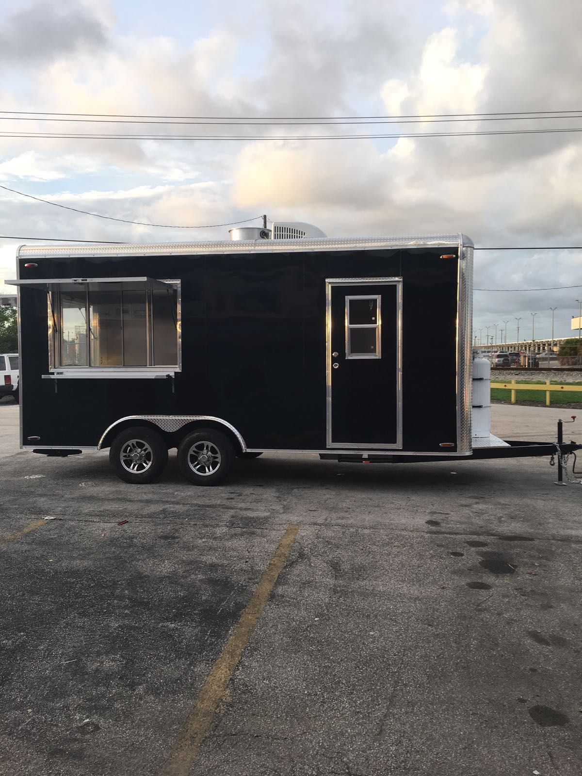 Black mobile trailer with serving window and side door parked on gravel under a cloudy sky