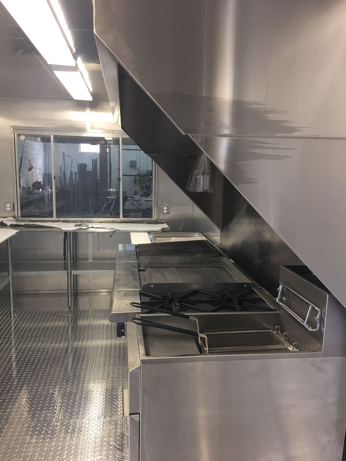 Stainless steel commercial kitchen with counters, sinks, and a glass door at the far end.