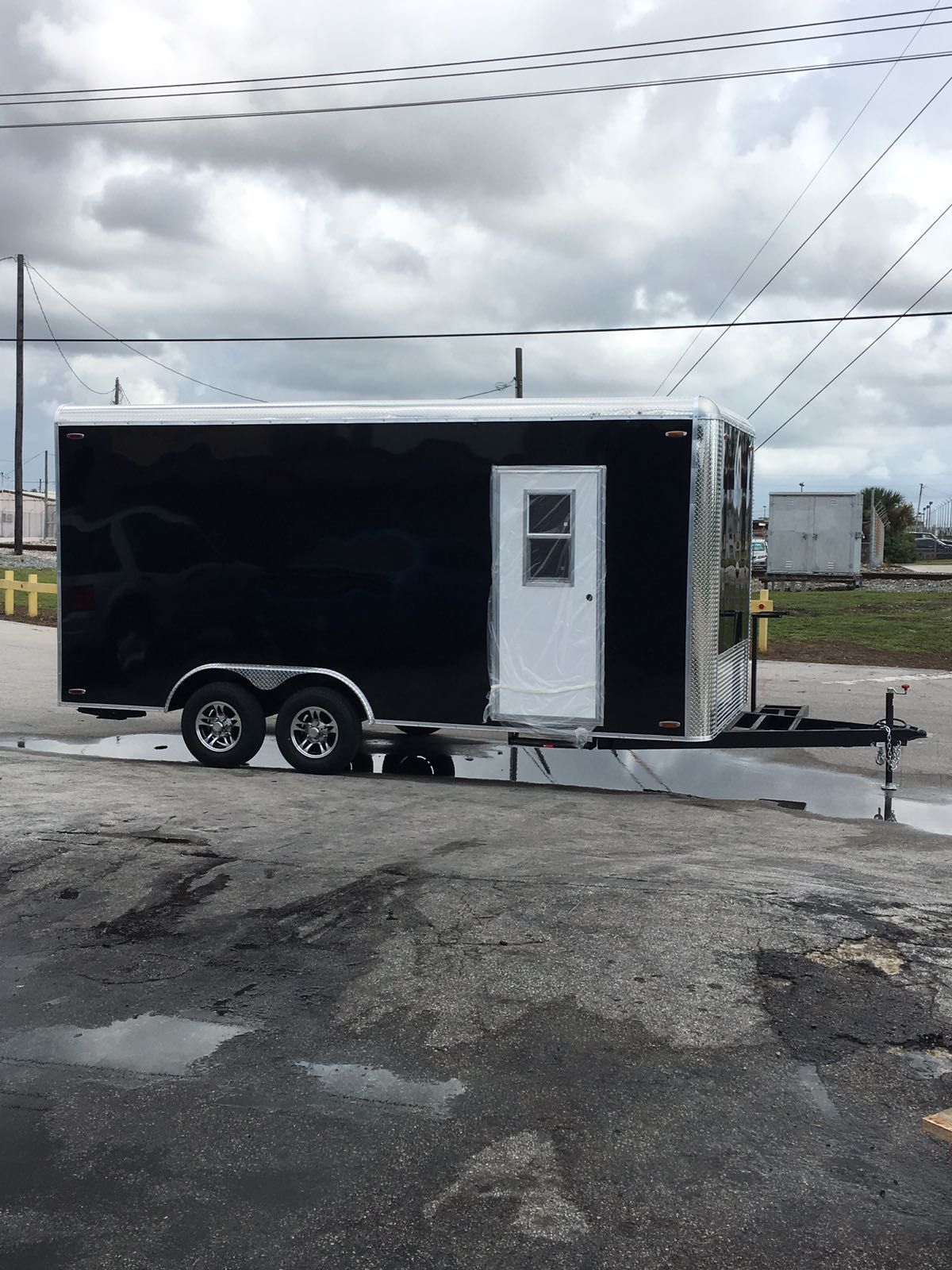 Black enclosed trailer with white door parked on gravel under a cloudy sky