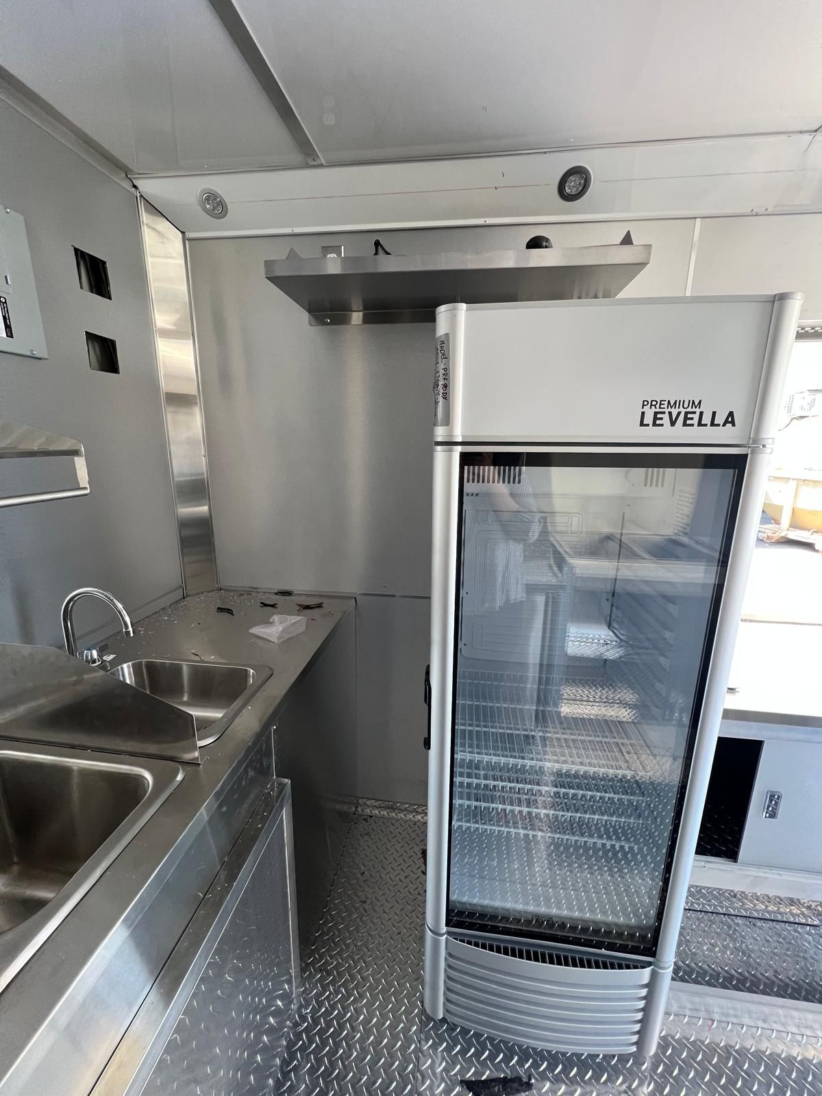 Commercial kitchen with stainless steel sink and counters beside a glass-door refrigerator.