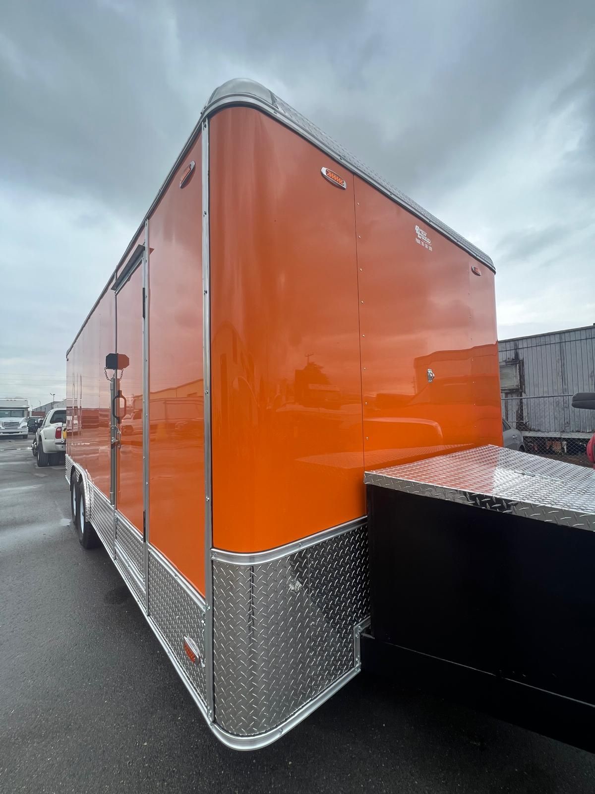 Orange enclosed trailer with silver trim parked in a lot, viewed from the rear corner.