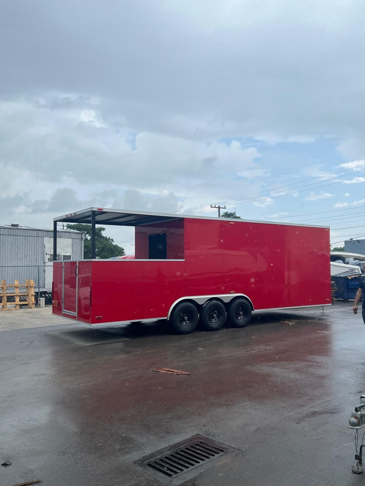 Red mobile trailer kiosk with open canopy, parked on wet pavement under cloudy sky.