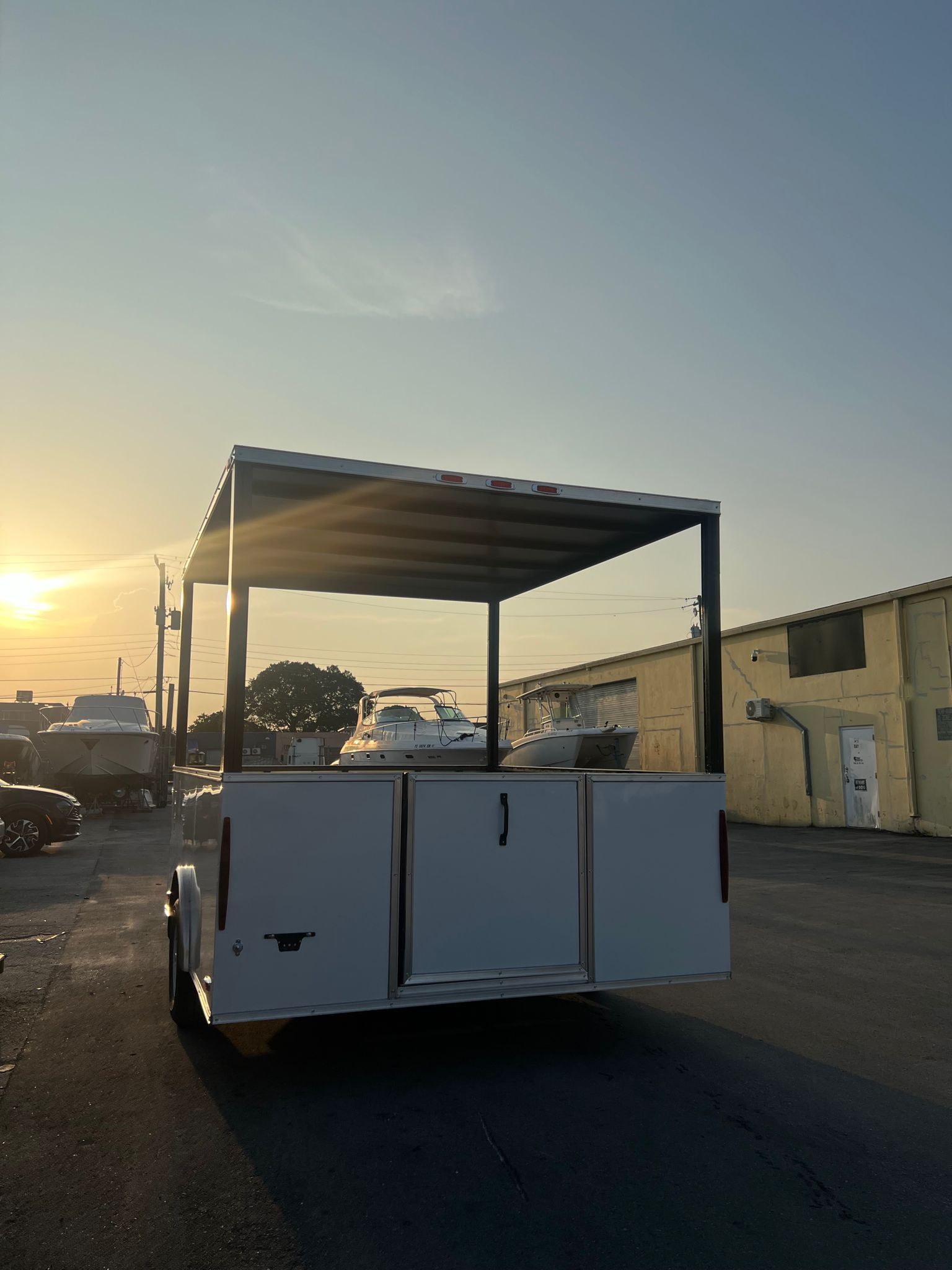 White utility cart with roof parked on a road at sunset beside industrial buildings