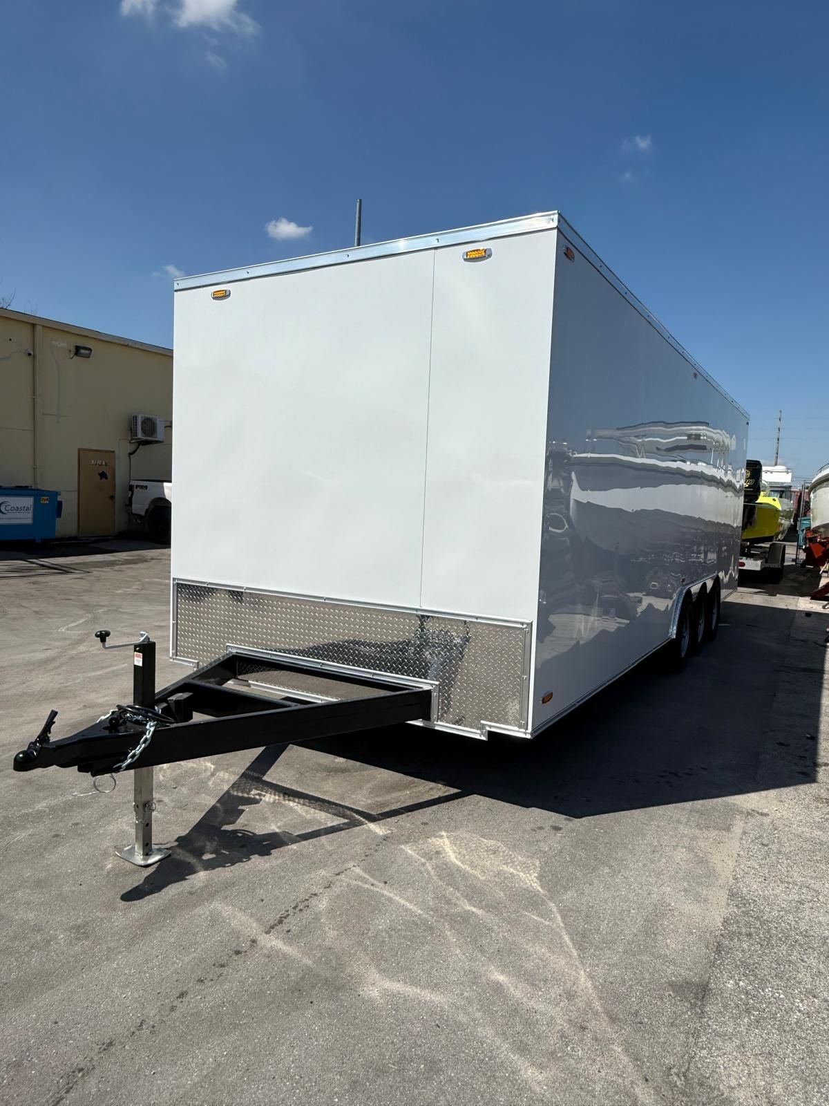 White enclosed trailer parked in an industrial lot under a clear blue sky