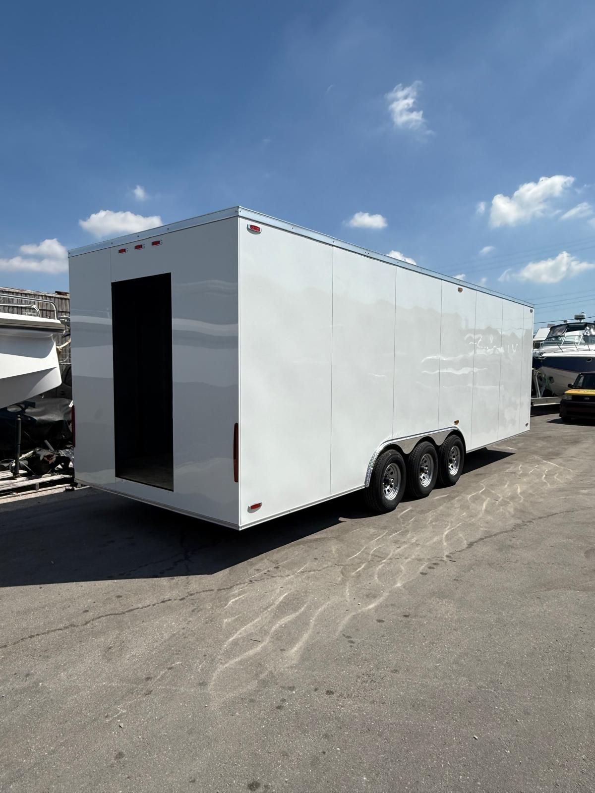 White enclosed triple-axle cargo trailer parked outdoors under a blue sky.