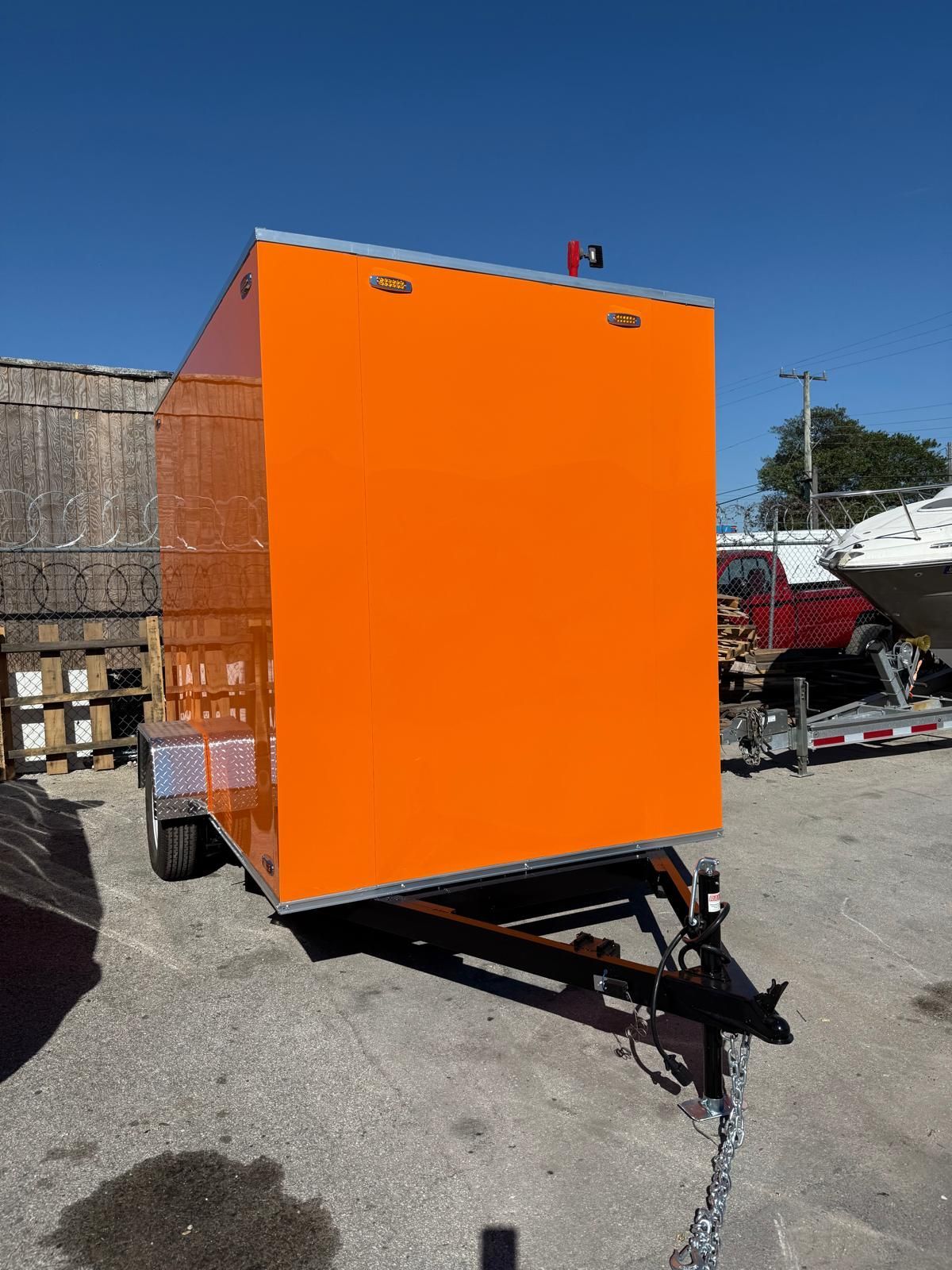 Bright orange utility trailer parked outdoors in a gravel lot