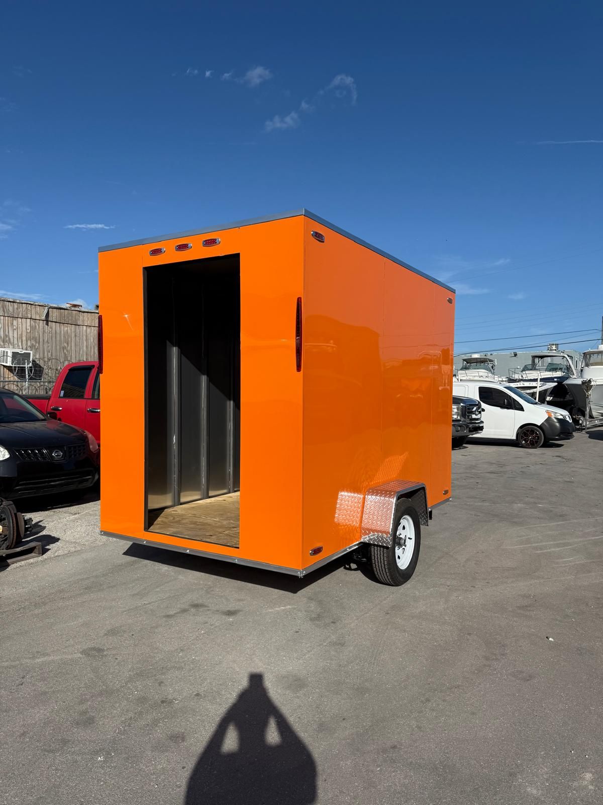 Bright orange cargo trailer with open door parked in a lot under a clear blue sky