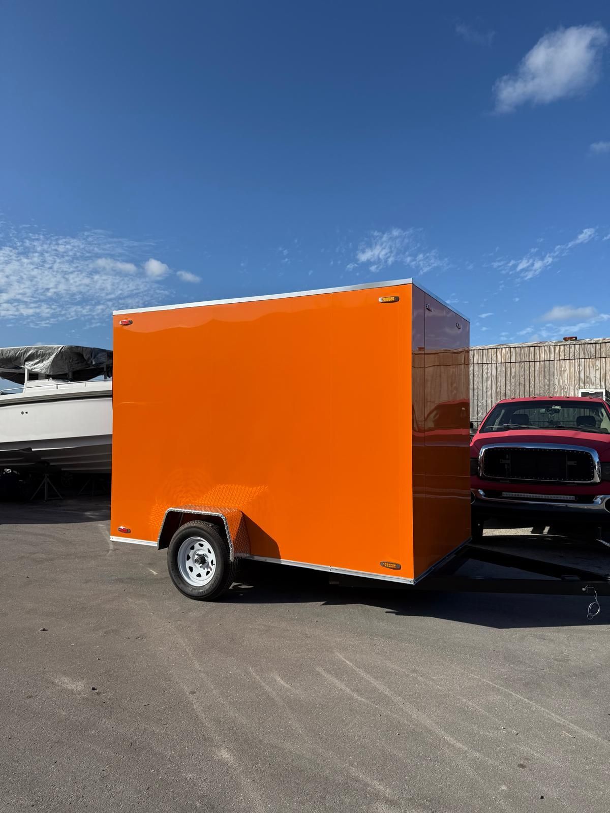 Bright orange enclosed cargo trailer parked on an asphalt lot under a blue sky